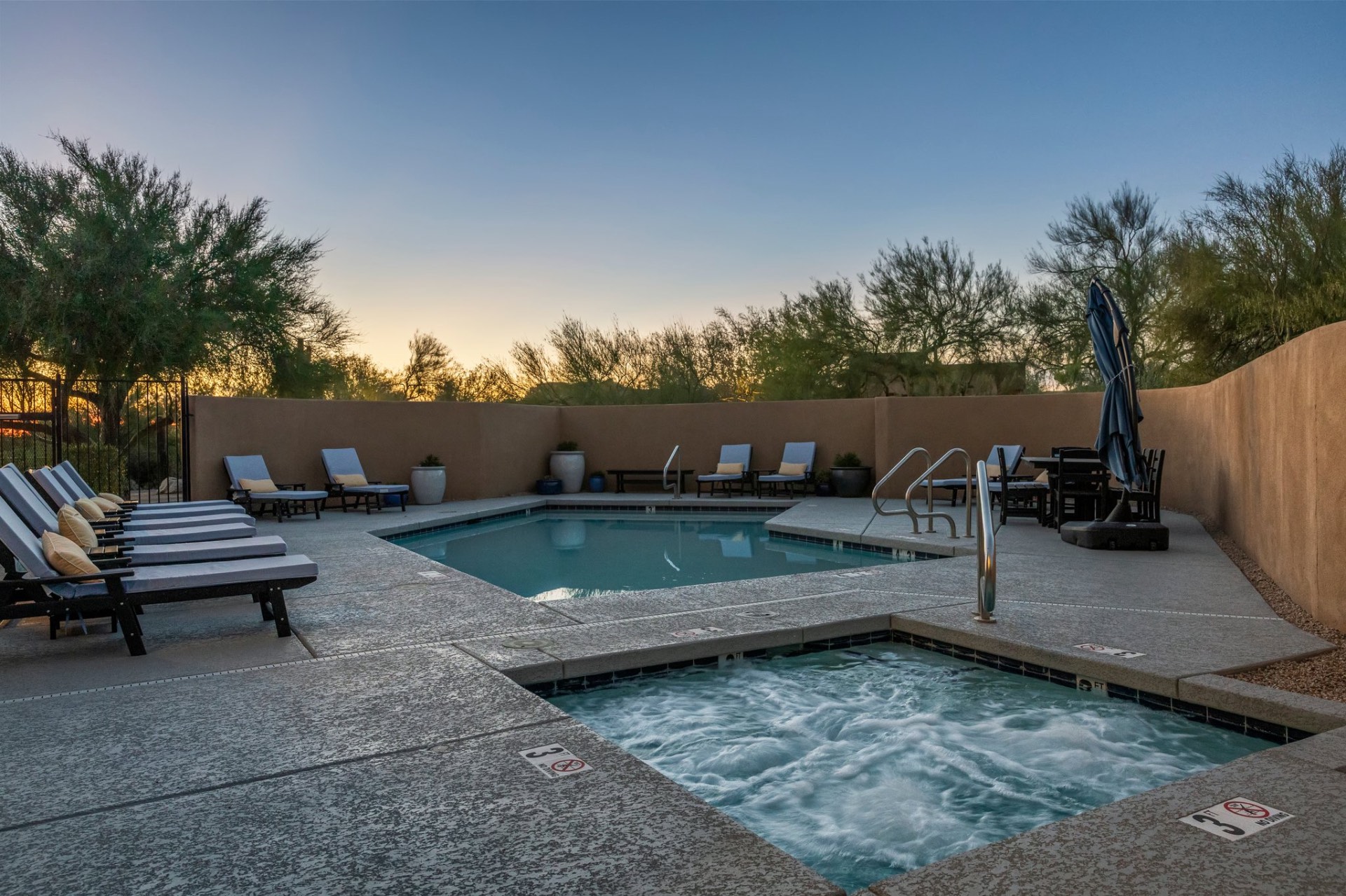 Heated resort pool and spa at sunset with chaise lounges and desert backdrop